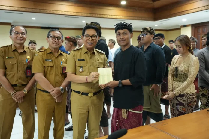 Bupati Adi Arnawa saat menyerahkan buku rekening tabungan kepada 26 Sekaa dan Komunitas Seni yang akan menjadi Duta Kabupaten Badung pada PKB XLVIII Tahun 2026, di Puspem Badung, Senin (13/4).