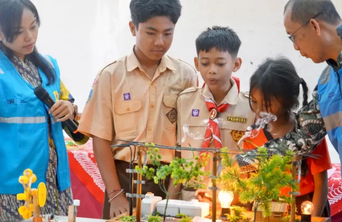 Perwakilan anak anak SD N 1 Tumbak Bayuh menyaksikan alat peraga simulasi terjadinya gangguan di jaringan listrik akibat gesekan pohon/material layangan pada saat pelaksanaan edukasi.